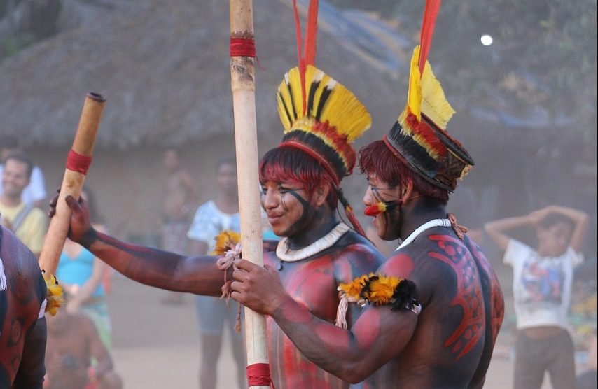 Dois homens indígenas e instrumentos musicais.