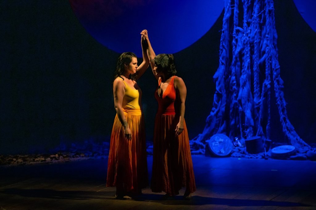 Duas mulheres no palco, com mãos dadas e ao alto.