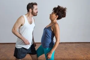 Um homem branco, de camiseta regata, enfrenta uma mulher negra, também de camiseta regata.