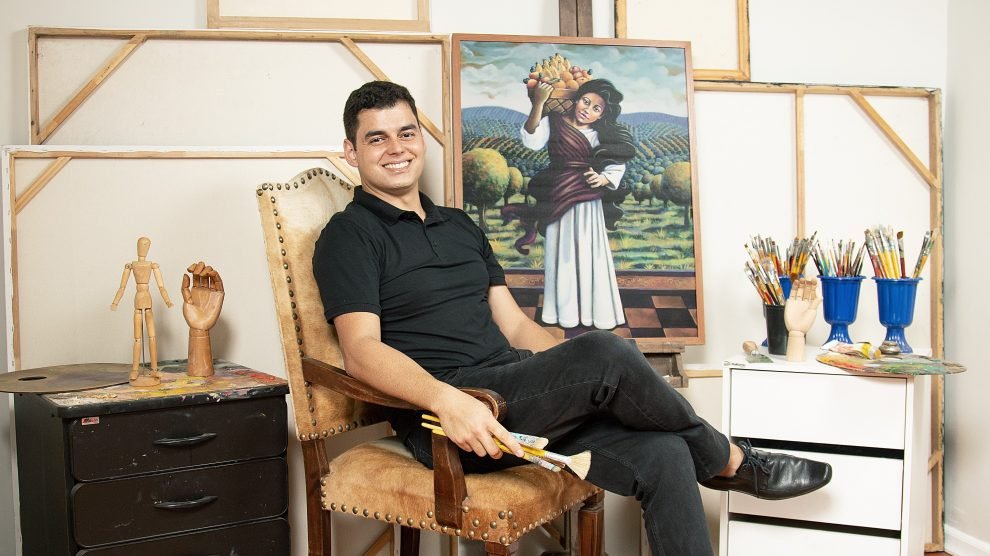 Homem, em uma sala, com obras de arte. Diego Mendonça recebe o Prêmio Top Of Mind